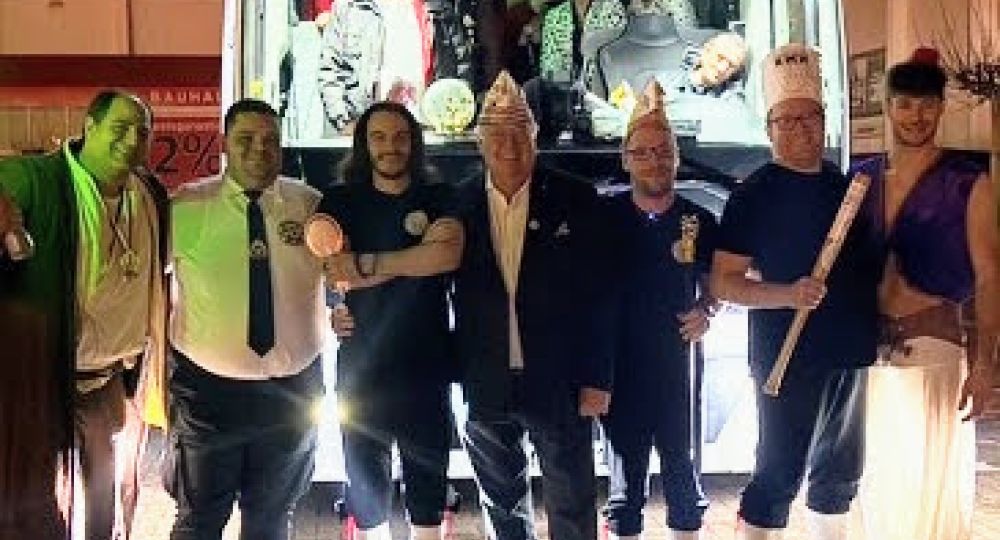 Das Foto zeigt eine fröhliche Gruppe vor einem Reisebus mit der Aufschrift „Rheinland-Touristik“. Im Vordergrund stehen mehrere Personen in karnevalistischer Kleidung, einige mit typischen Narrenkappen.