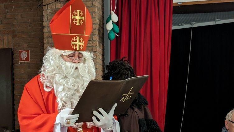 Eine als Nikolaus verkleidete Person mit rotem Gewand und Bischofsmütze liest aus einem großen Buch vor.