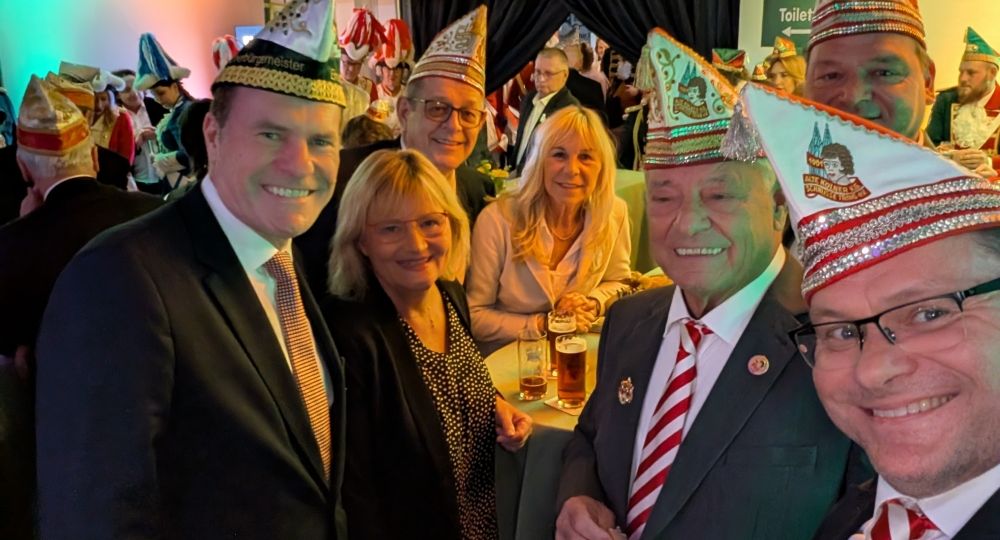 Mehrere festlich gekleidete Personen feiern in fröhlicher Stimmung – viele tragen traditionelle Karnevalsmützen der Alte Kölner K.G. „Schnüsse Tring“, passend zur jecken Atmosphäre.